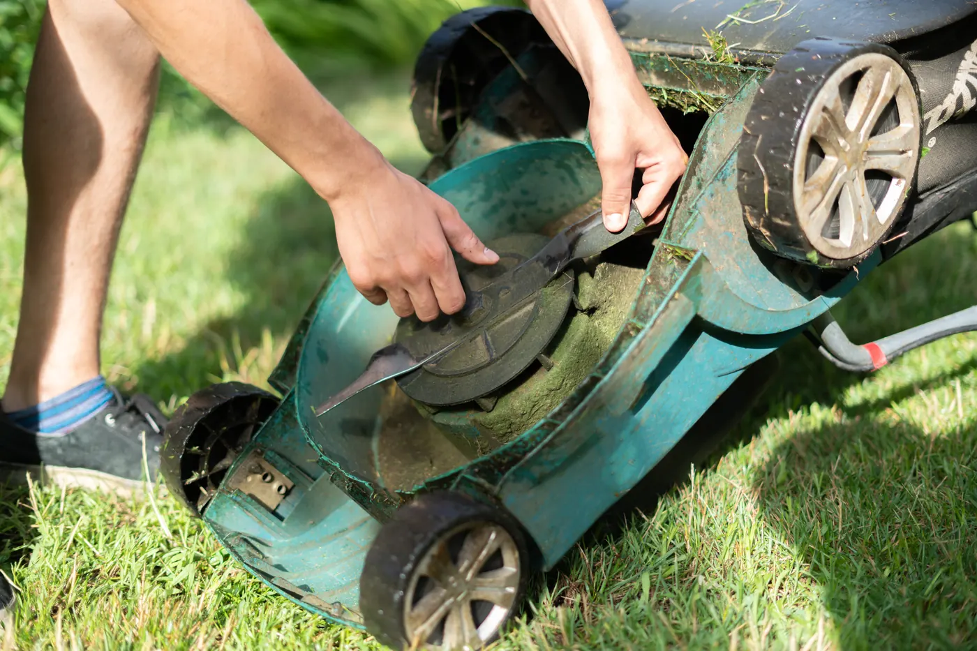 Hands working on the underside of a lawn mower